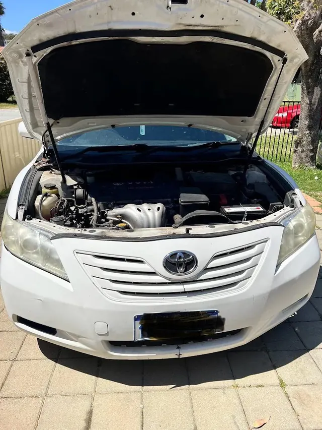White Toyota Camry with the bonnet up and the engine bay open on a paved driveway